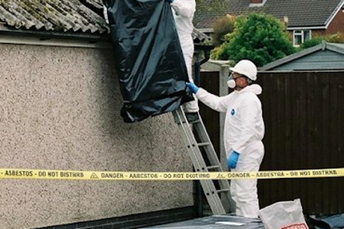 Operative wetting an old asbestos cement roof with a hand sprayer before removal